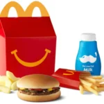 A McDonald's Hamburger Happy Meal featuring a classic hamburger, World Famous Fries® (Kids), a 1% Low Fat Milk Jug, and fresh apple slices, served in the iconic Happy Meal box.